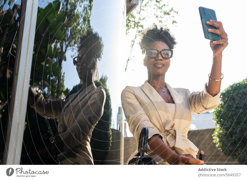 Smiling black Businesswoman in eyeglasses using mobile phone while taking selfie manager beautiful smartphone lipstick low angle wall reflection cellphone