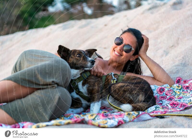 Woman with pet resting at beach tourist woman dog lying sand happy sunglasses adorable smile blanket relax vacation cheerful beautiful animal looking at camera