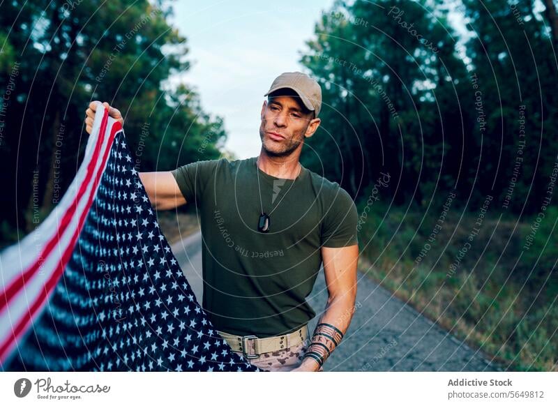 Military soldier holding and looking at national flag with pride while standing on road against forest man commando american uniform special force enforcement