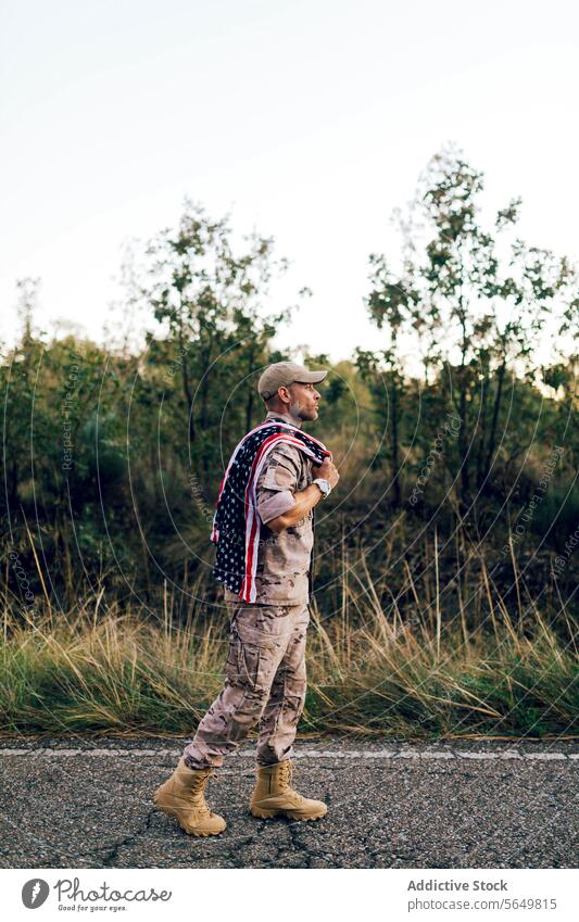 Side view of Mature commando with American flag on shoulder on road under sky at sunset soldier american walking camouflage uniform plant brave full body ranger