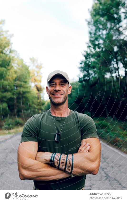 Smiling military soldier wearing uniform standing on road while looking at camera man commando smiling confident portrait hero arms crossed tattoo sky green