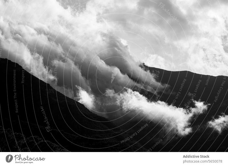 Dramatic clouds enveloping a mountain in monochrome black and white dramatic atmospheric rugged contour nature landscape intensity swirling darkness contrast