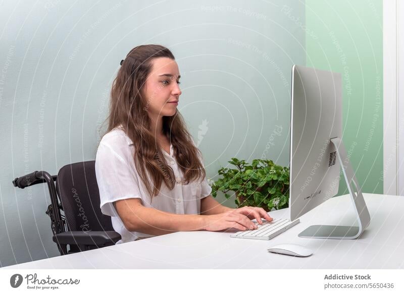 Young professional working in wheelchair at computer in office woman modern bright young desk job technology business concentrate focus employee career