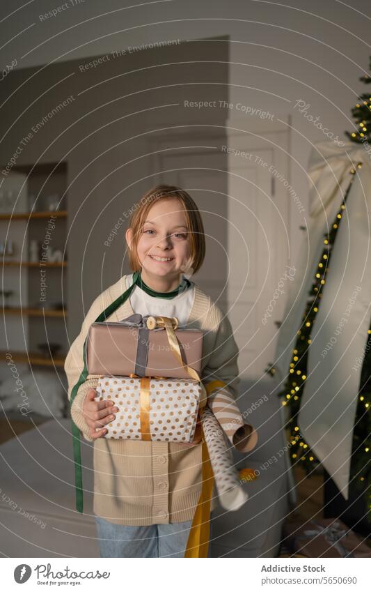 Smiling girl holding gifts by a Christmas tree christmas present decoration festive holiday smiling child cheerful joy happiness wrapped wrapping paper ribbon