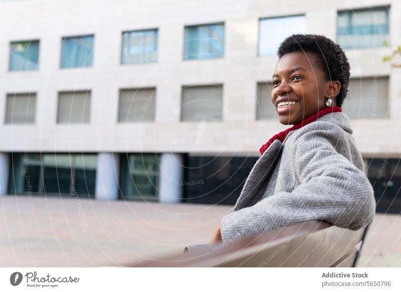 Cheerful black woman relaxing on bench rest city weekend free time town autumn street park enjoy satisfied smile happy cheerful female adult african american