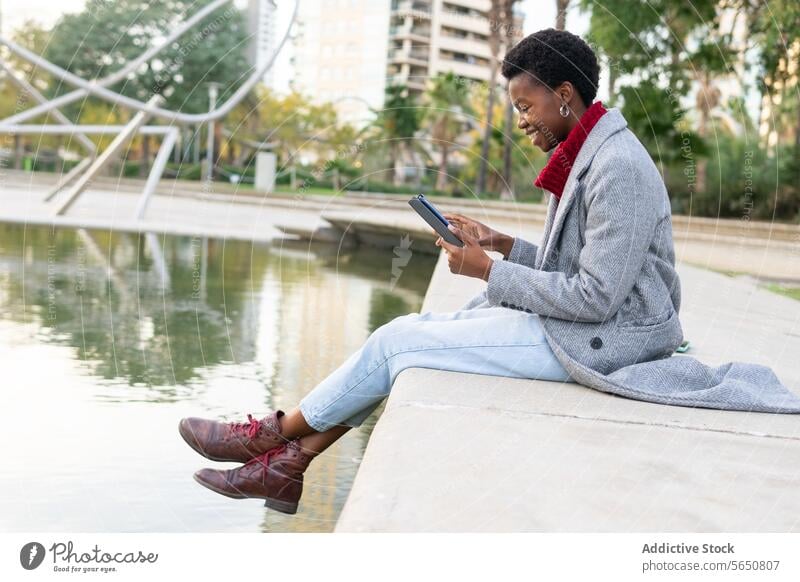 Side view of black woman reading electronic book in park using digital book e book city pond smile positive happy enjoy female adult african american ethnic