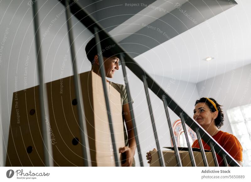 Smiling mother and son carrying boxes in new building move in cardboard together smile apartment relocate home real estate belonging property happy house boy