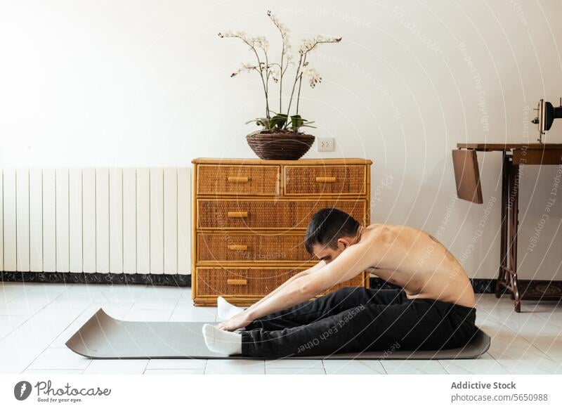 Focused young man sitting on mat and stretching legs during workout at home rehabilitation practice yoga meditate session mindfulness stress relief vitality