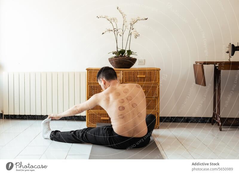 Focused young man sitting on mat and stretching leg during workout at home rehabilitation practice yoga meditate session mindfulness stress relief vitality