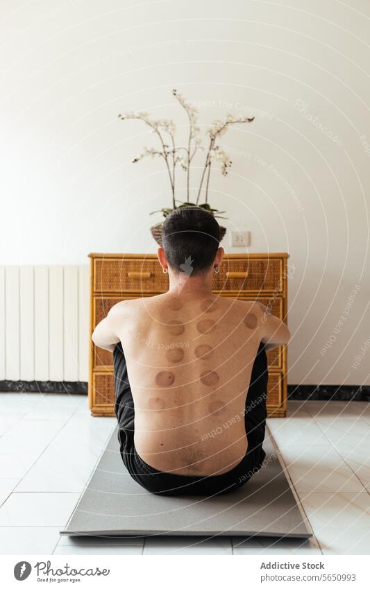 Anonymous shirtless man sitting on yoga mat exercise rehabilitation mark physiotherapy back wellness care home practice activity male young body healthy