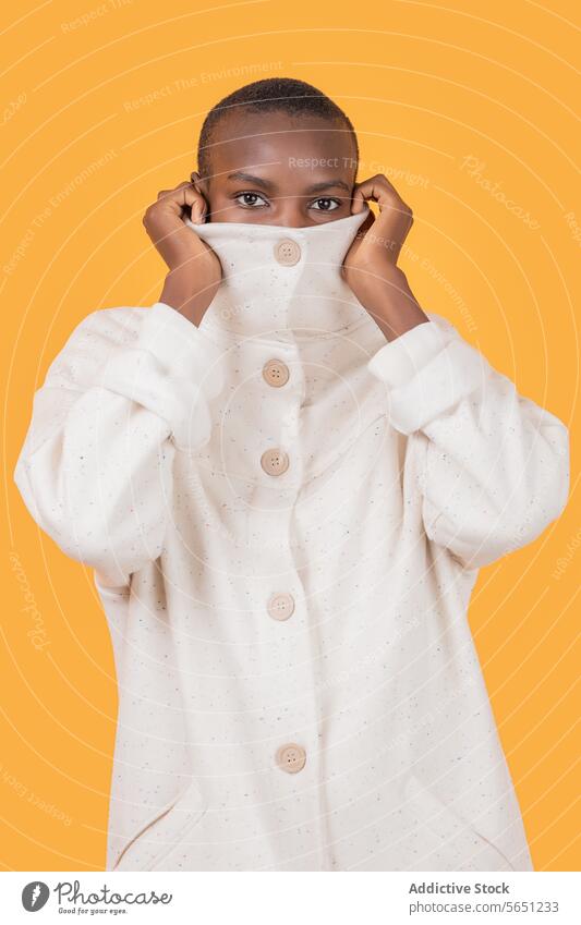 Black woman in turtleneck clothing isolated on yellow background trendy apparel covering mouth face portrait short hair staring confident style glance