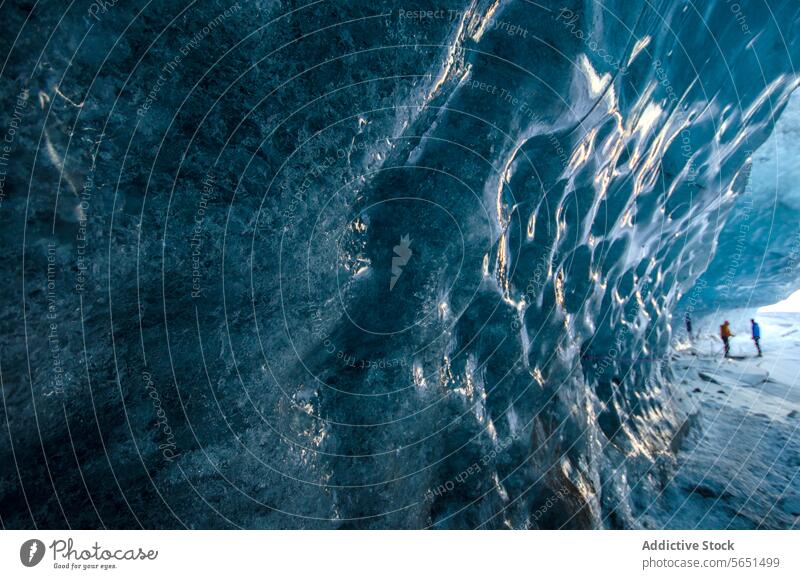 Close-up of textured blue ice inside a cave with silhouettes of people in the distance in Iceland ice cave glacier person close-up detail frozen arctic