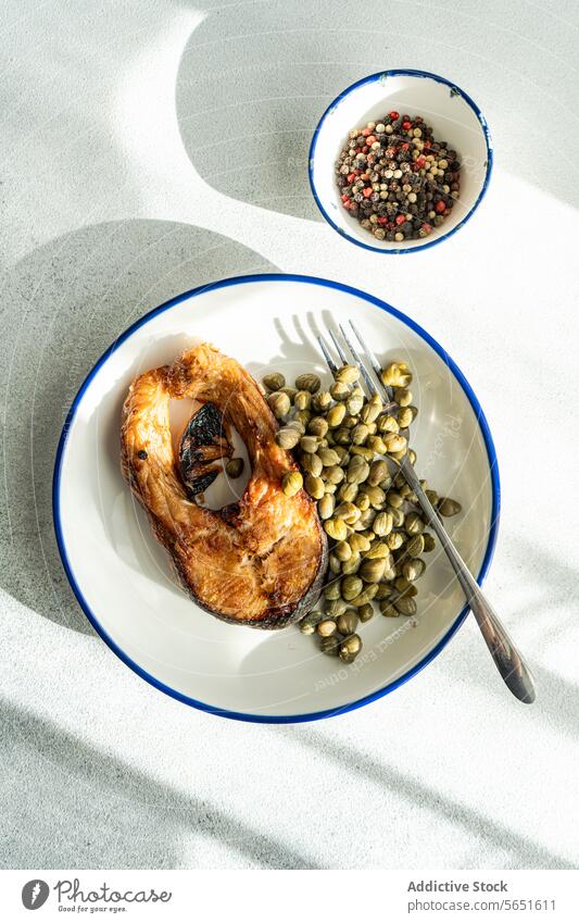 Top view of Grilled Trout Steak on a Plate with capers placed on table near bowl trout steak grilled plate white blue rim garnish wedge flavor dining casual