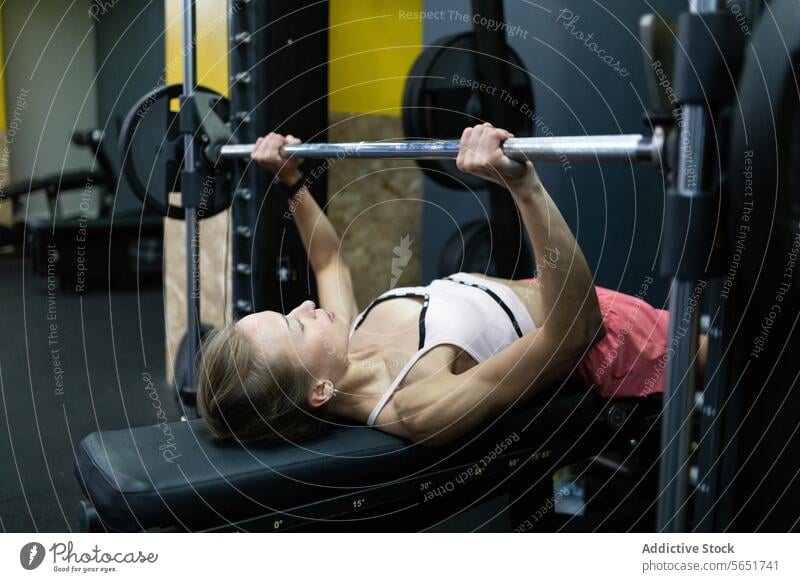 Fitness enthusiast woman performs bench press in gym fitness workout exercise barbell lifting health sport strength training athlete focus determination