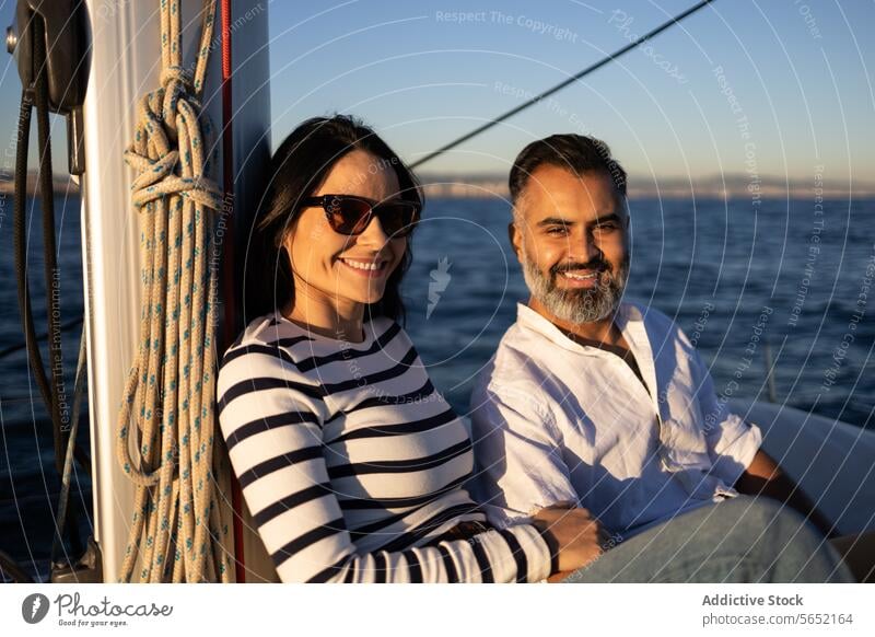 Smiling couple sitting on yacht smile pleasure enjoy relax sea happy trip romantic peaceful lifestyle casual adventure paradise embrace hug sailboat tourism