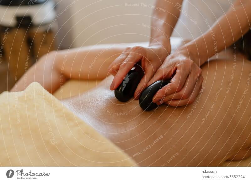 Close-up of hot stone massage therapy on a bare back with therapist’s hands at a beauty salon or hotel asian therapist's hands relaxation wellness heated stones