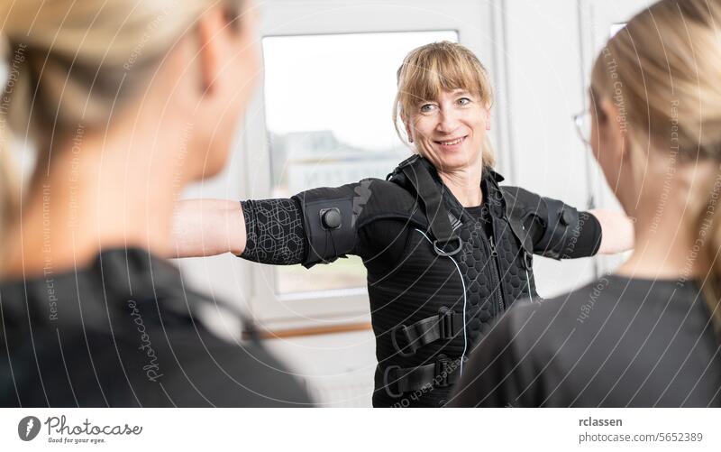 woman is being assisted with fitting an EMS training suit by a trainer in a modern EMS-Studio electro stimulation neuromuscular electrical endurance