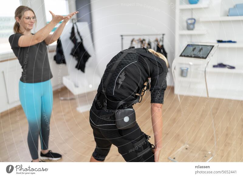 Woman in EMS suit performing exercises with trainer guidance and computer in a EMS - Studio electro stimulation neuromuscular electrical body sculpting ems suit