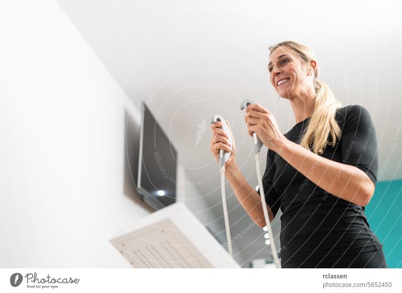 Client smiling holding grips of a body composition measuring scale for Inbody test in a fitness center, with a blurred background. inbody fat fitness technology