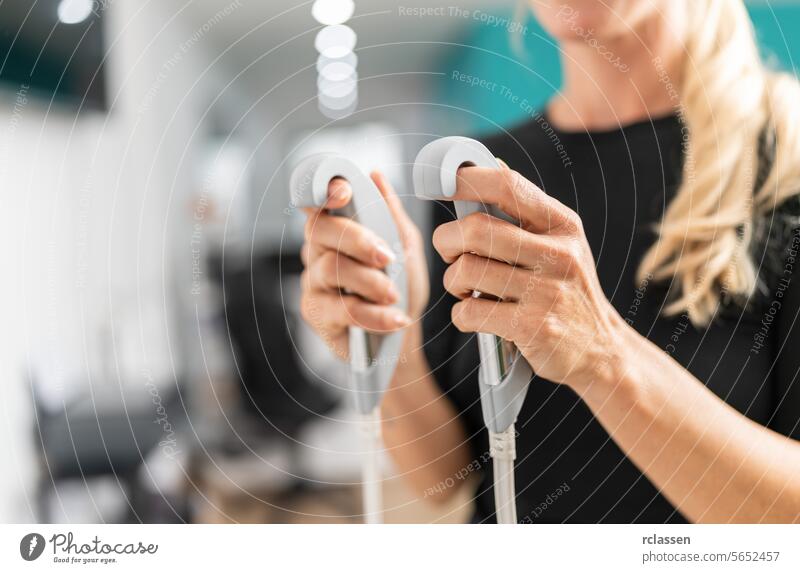 Close-up of a woman's hands holding the handles of a body composition measuring scale analyzer in a fitness studio setting. inbody fat analyzing bioelectric bmi