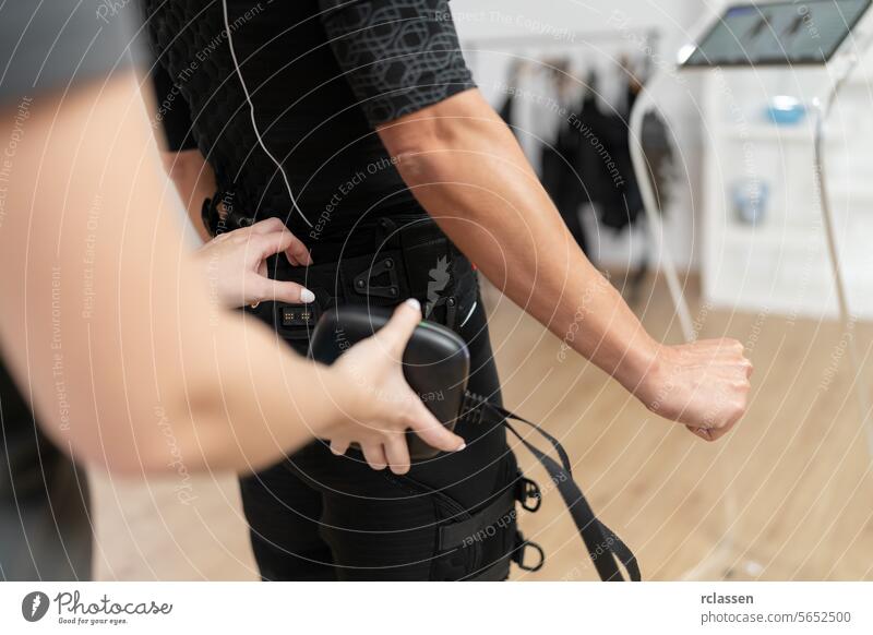 Close-up of a trainer adjusting an EMS suit on a woman in a gym, adding a battery pack for training in a EMS - Studio electro stimulation neuromuscular