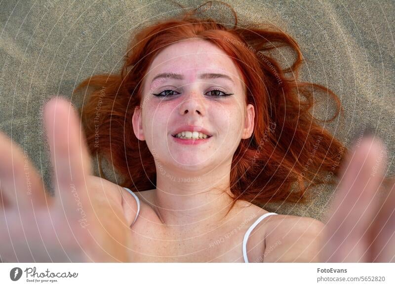 Laughing young woman from above, lying in the sand, arms up portrait freckles cute dress European beauty female attractive dune beach sandy beach outdoors