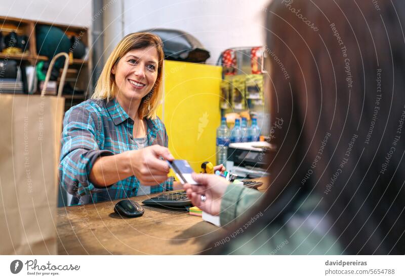 Smiling woman shop assistant taking credit card of client to charge purchase. Local commerce concept smile customer cheerful cashier employee female store serve