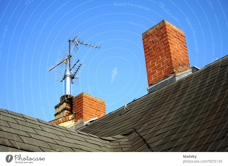 Red brick chimney and old television aerials on an old building against a blue sky in the sunshine in the north end of Frankfurt am Main in Hesse North End Roof