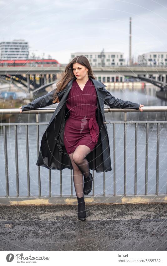 relaxed young woman in a black coat stands on a bridge Woman Meditative sensual Dreamily self-aware Elegant emancipated urban fortunate youthful fashion Longing