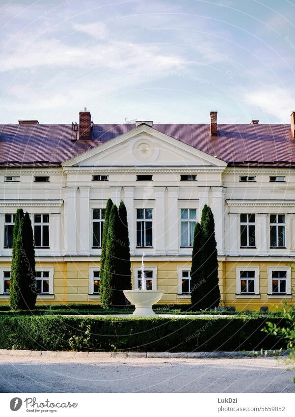 Photo of the facade of a classical palace surrounded by green trees with a fountain in front of it on a sunny summer day with no people history infrastructure