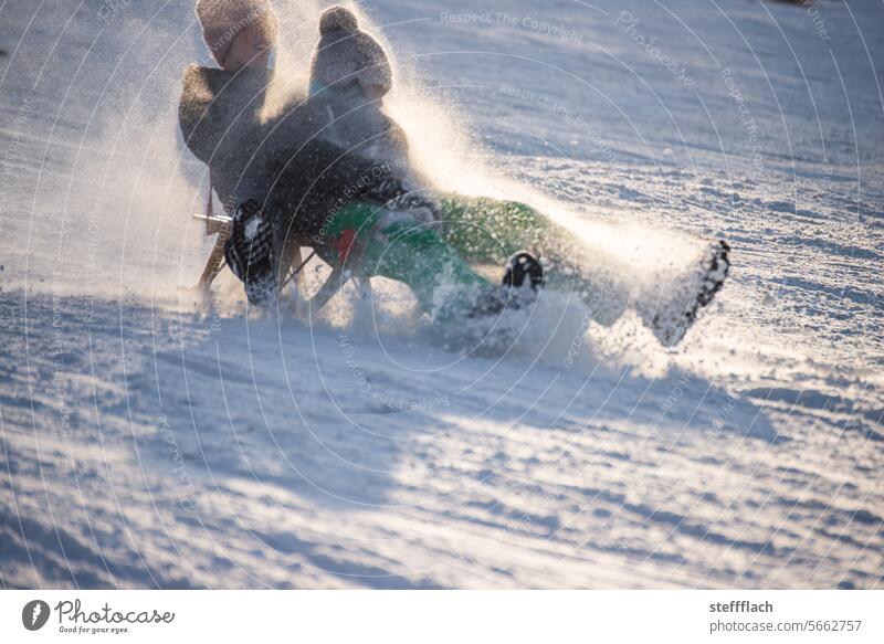 Two children race through the sunshine on a sled, dusted with snow Snow Winter Sleigh sledging Child Sunlight Sledding Sledge Toboggan run Cold Ski piste