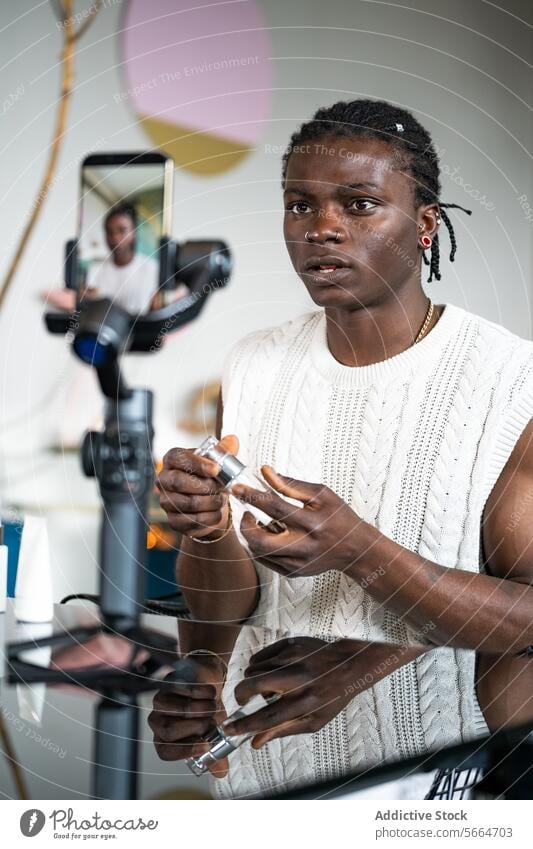 Focused black man in a white sweater explains product features while filming a skincare tutorial product explanation smartphone gimbal broadcasting vlogging