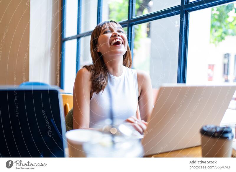 Cheerful Asian woman enjoying a remote work session in a cafe, with a bright window backdrop in Chiang Mai, Thailand cheerful happy technology business smile