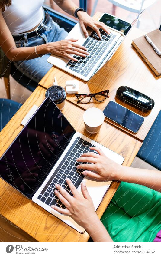 From above view of unrecognizable colleagues using laptops in a cafe, with smartphones and coffee cups on the table, showcasing a collaborative remote work atmosphere in Chiang Mai, Thailand