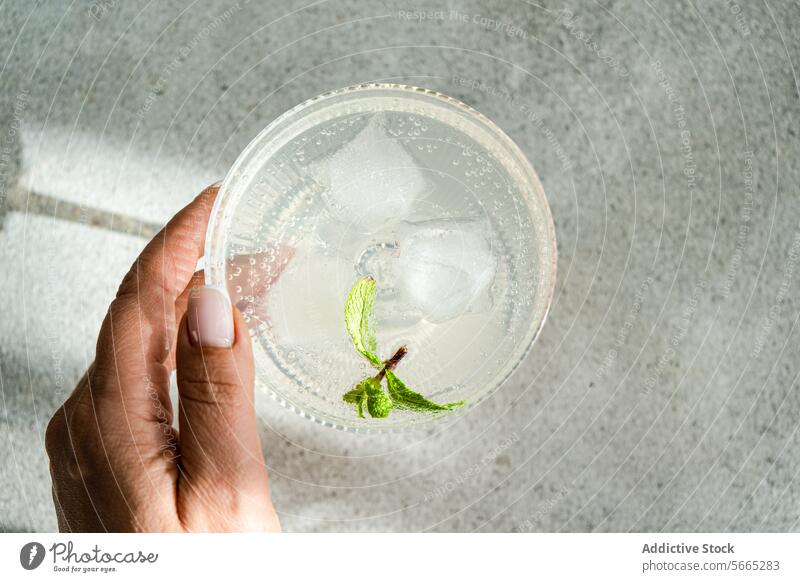 Refreshing drink with lime and mint in a glass held by hand ice vodka fresh mint leaves cube of ice refreshment transparent close-up beverage cold citrus herb