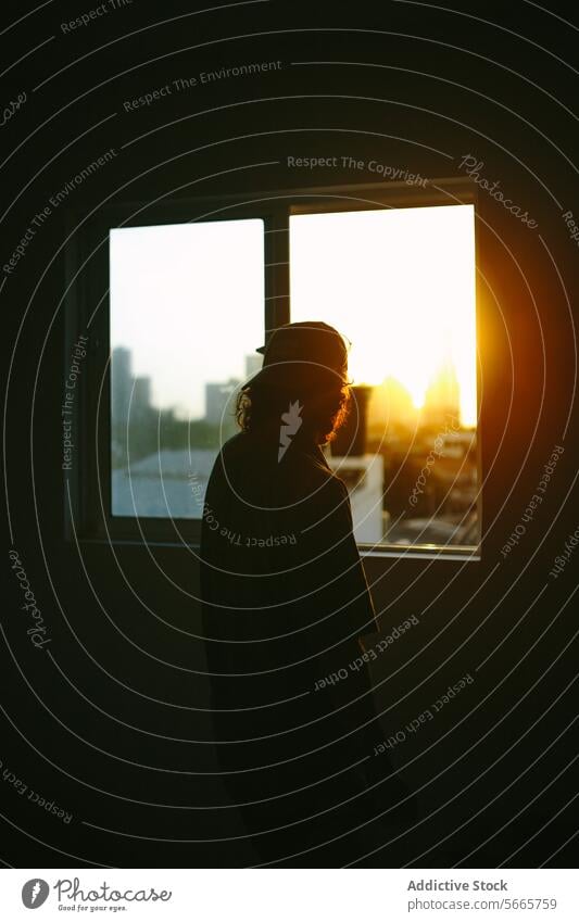 Silhouette of person gazing at sunset through window silhouette twilight warm glow contemplative individual framed geometry scene indoors shadow dusk profile