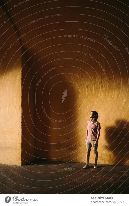 Man standing alone in sunlit corner with deep shadows in Cartagena, Colombia man sunlight wall warm tone contemplative young contrast solitude quiet peaceful