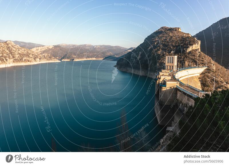 A dam nestled between mountainous terrain with a reservoir displaying low water levels indicative of drought conditions water shortage scarcity hydroelectric