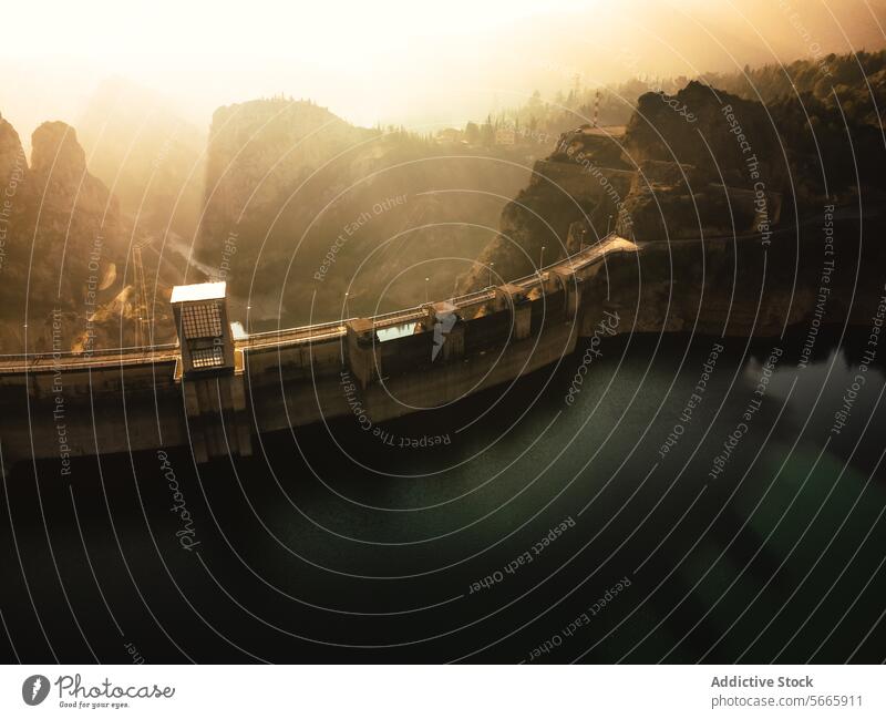 From above of golden sunlight filters through haze over a dam enclosed by steep cliffs and tranquil waters reservoir hydroelectric infrastructure landscape