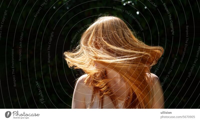 wide panorama banner of unrecognizable beautiful sexy redhead woman ginger portrait, shaking her flying long red hair against the dark ivy background in sunny backlight