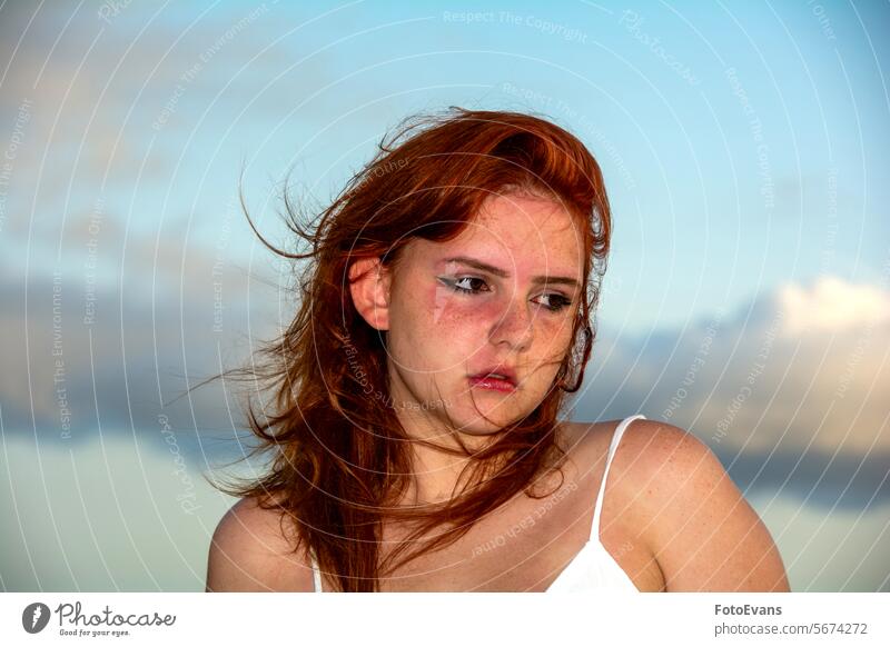 Young woman with windblown hair and sky portrait Active cute dress European young windy female attractive summer girl sandy beach outside sunburn face