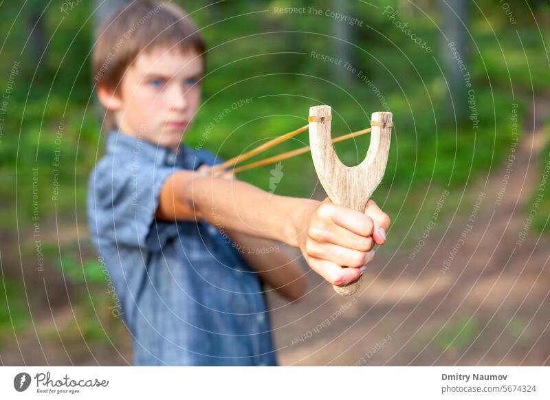 Kid with slingshot accuracy activity aim arm bad bean shooter behavior boy brat caucasian child danger face flip fun game hand hand catapult holding hooligan