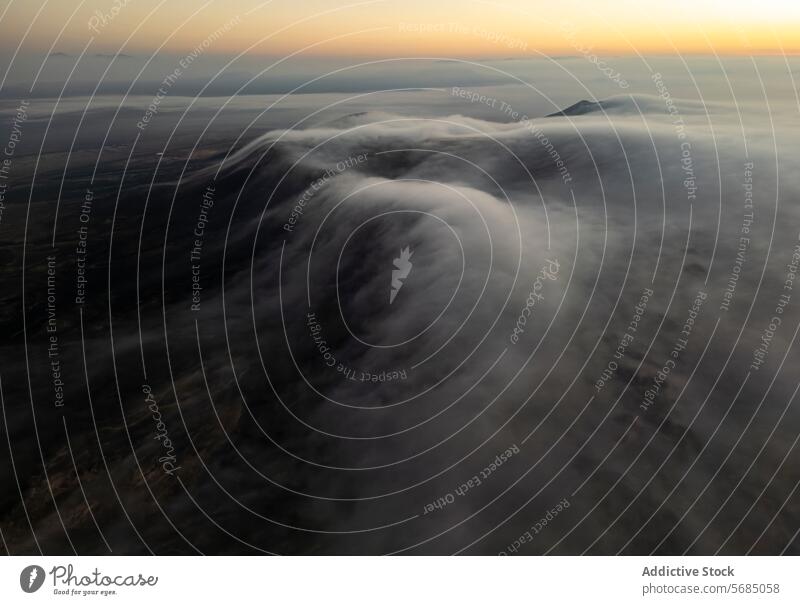 Soft clouds cascade over the darkened landscape of Fuerteventura as the first light of sunrise peeks over the horizon flow aerial dawn soft terrain nature