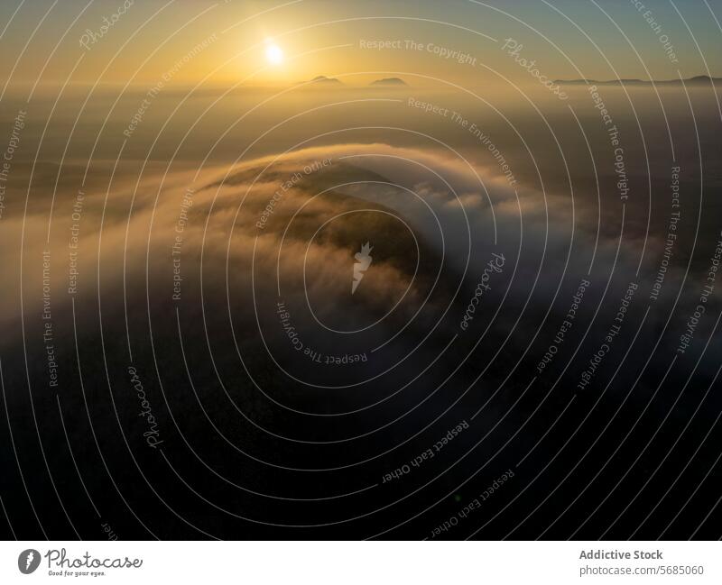 The sun peeks over the horizon, illuminating the mist-covered hills of Fuerteventura with a golden hue sunrise cloud illumination aerial landscape nature