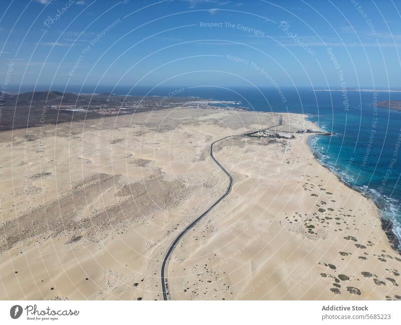 Top view of expansive view of a road meandering through Corralejo Dunes against a backdrop of ocean and clear skies in Fuerteventura Aerial desert sky coastal