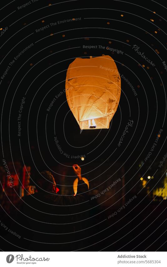 Glowing Sky Lantern Floating in Dark Night Sky sky lantern night glow dark silhouette person float light release festival tradition celebration luminescence