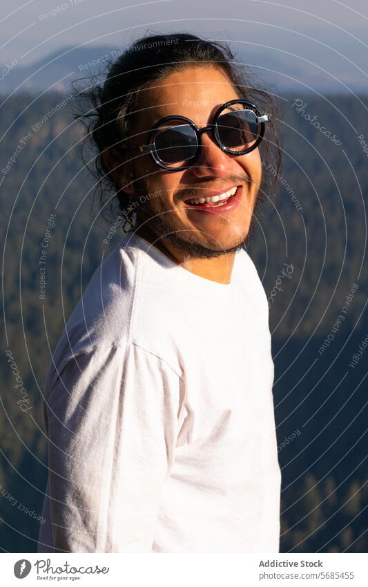 Happy young man standing in mountainside nature positive toothy smile beard casual happy cloth sunglasses wear travel trip enjoy male tourist optimist cheerful