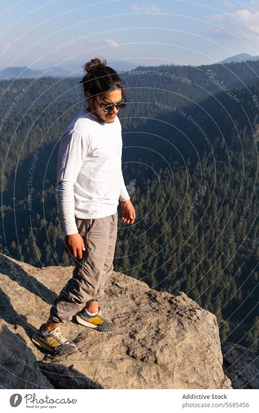 Brunet man standing on rocky cliff in highlands tourist admire mountain sneakers scenery pants traveler nature vacation tourism majestic landscape adventure