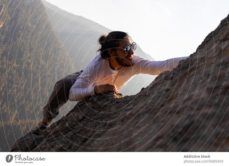 Brave young man climbing mountain cliff ridge positive brave sunglasses style cloth nature adventure highland travel male smile cheerful rough range happy