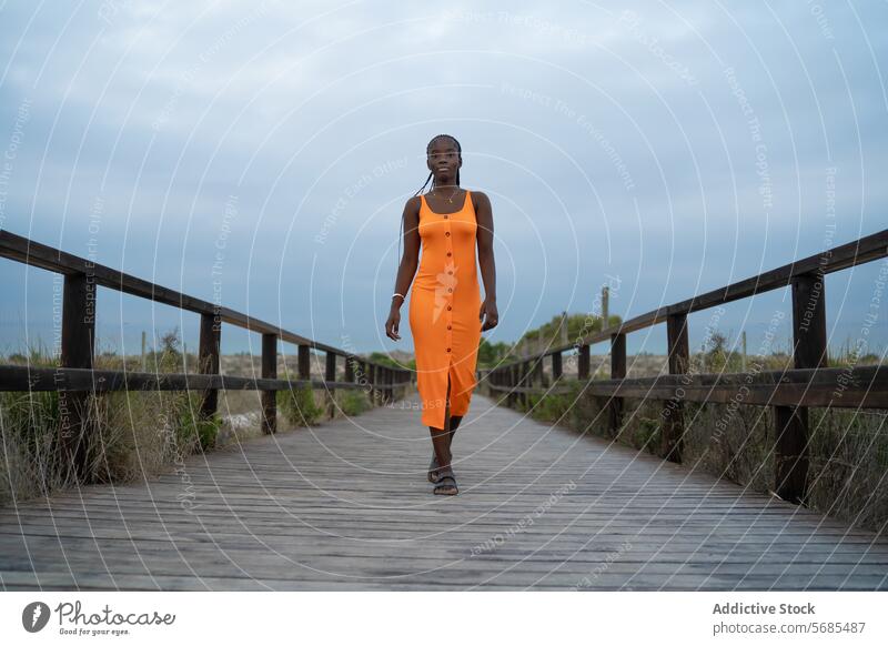 Serious black woman walking on wooden footbridge lady gown smile positive traveler hill mountain nature vacation female bush boardwalk trip dress journey green